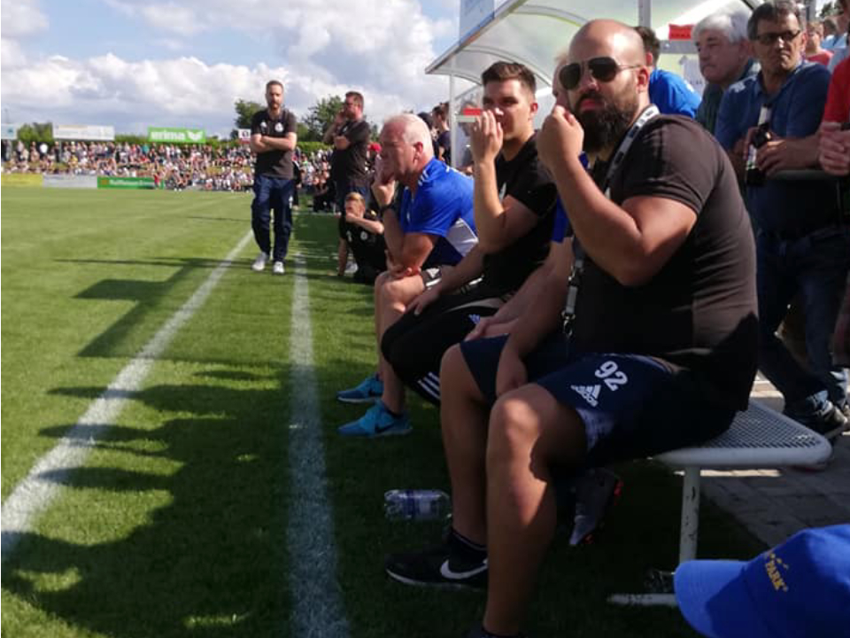 Eine Gruppe von Männern sitzt auf einer Bank bei einem Fußballspiel.