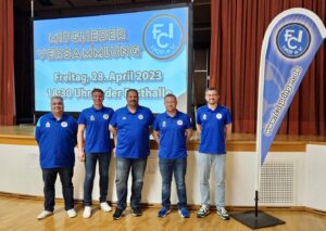 Vier Männer in blauen Hemden stehen vor einem Bildschirm und präsentieren Informationen.