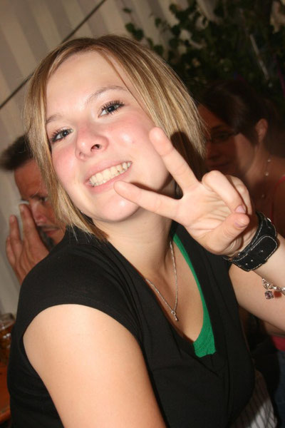 Eine Frau in einem schwarzen Shirt steht lächelnd vor einem neutralen Hintergrund.