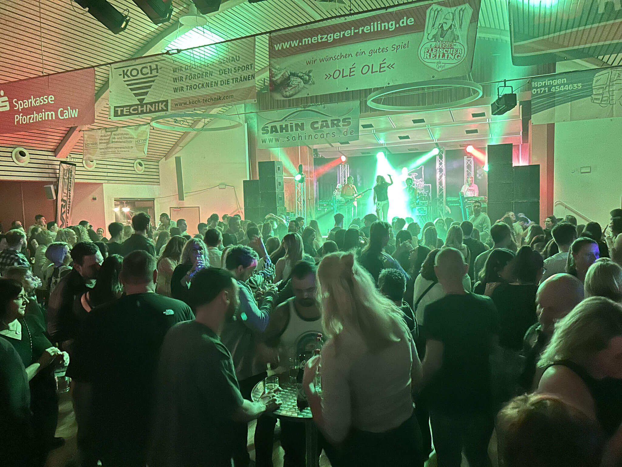 Eine große Menschenmenge feiert fröhlich auf einer Party, umgeben von bunten Dekorationen und Lichtern.