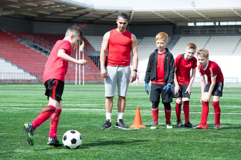 Junge Spieler und ihr Trainer versammeln sich um einen Fußball auf dem Spielfeld.